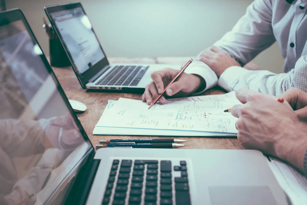 Two accountants working through notes and laptops at a shared desk