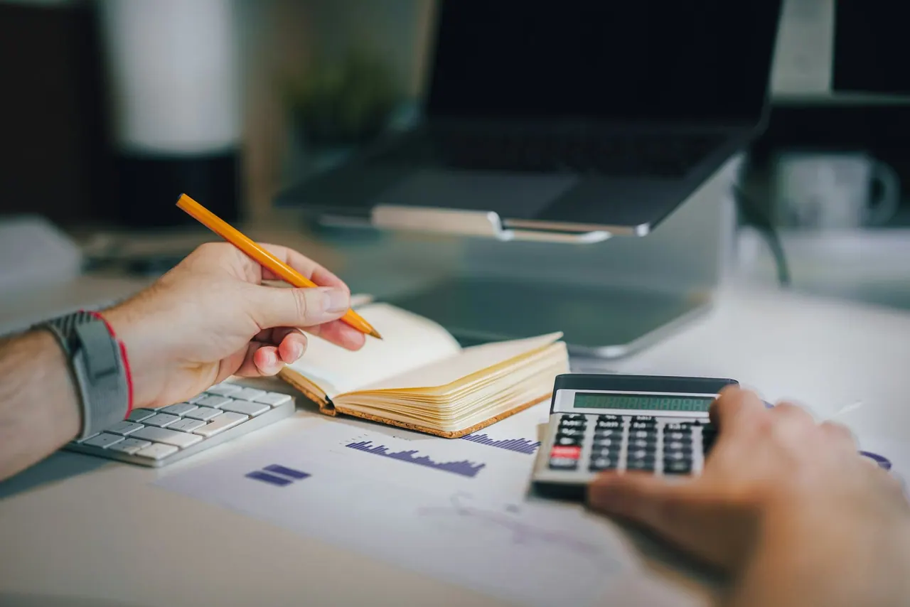 Hands working through figures with a pencil, a notebook and a calculator