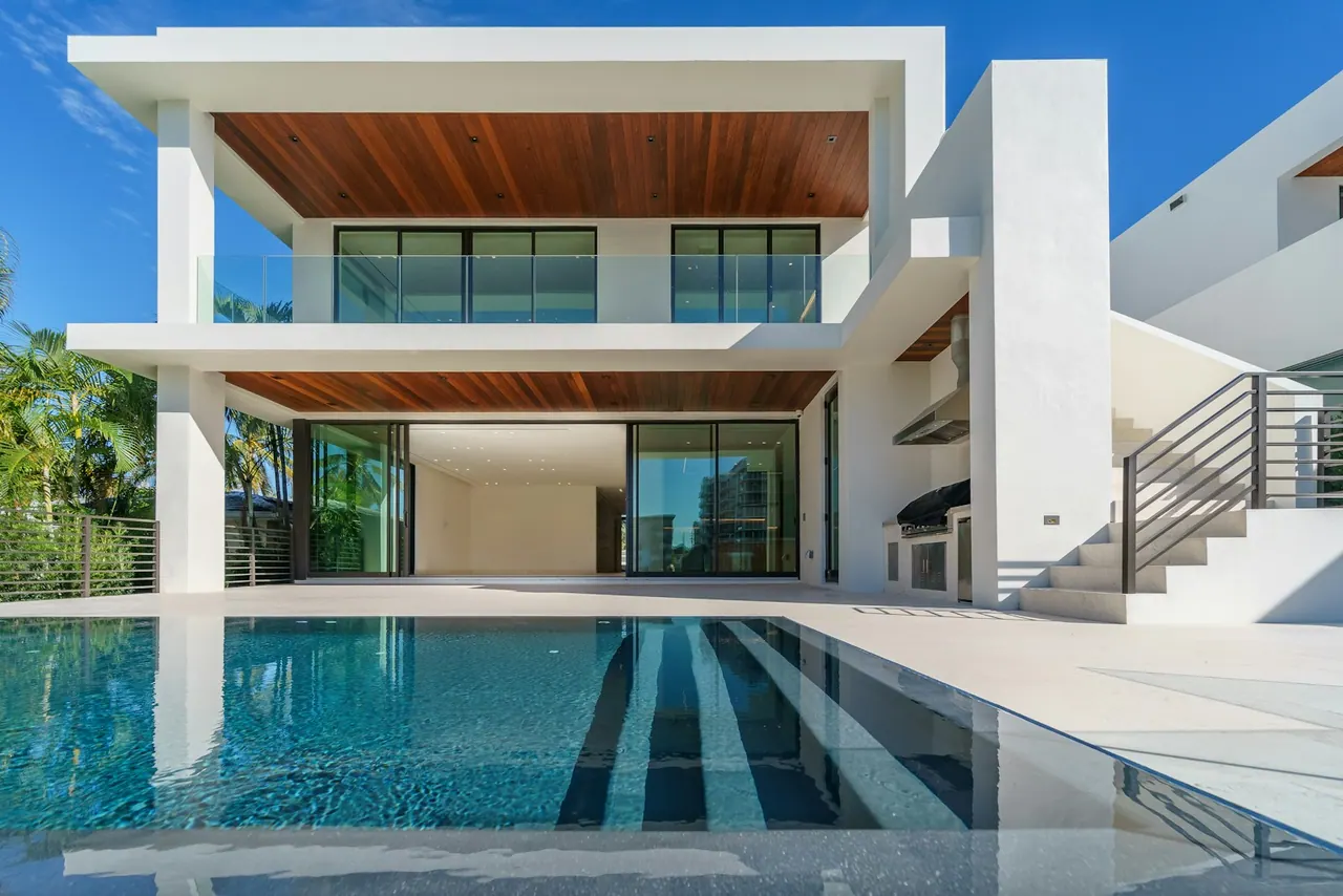 A white modern house with warm wood soffits above a long pool