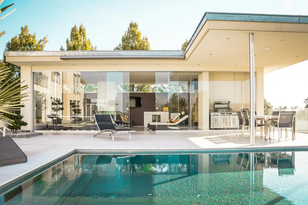 A glass walled house opening onto a pool