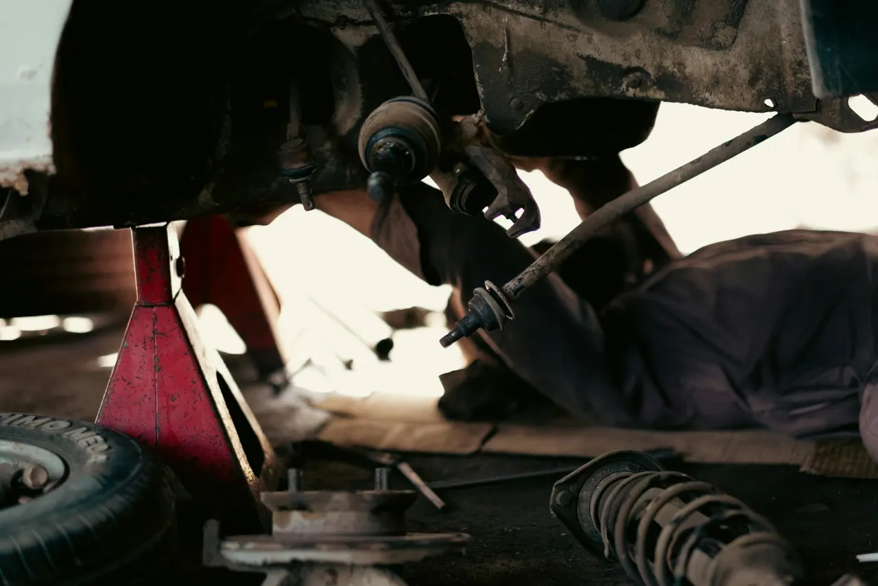 A mechanic lying under a raised car beside a jack stand