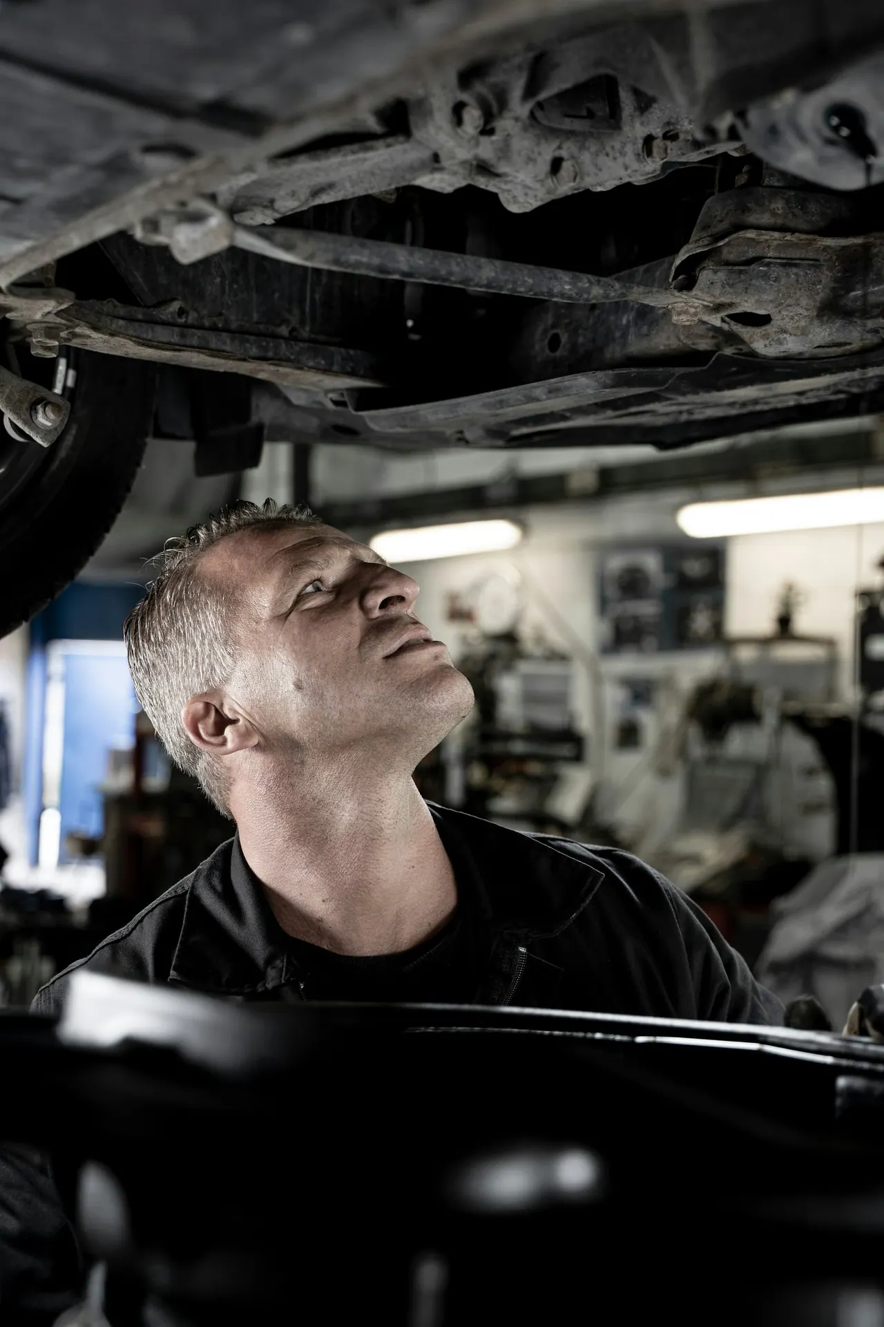 A technician looking up at the underside of a car on a lift