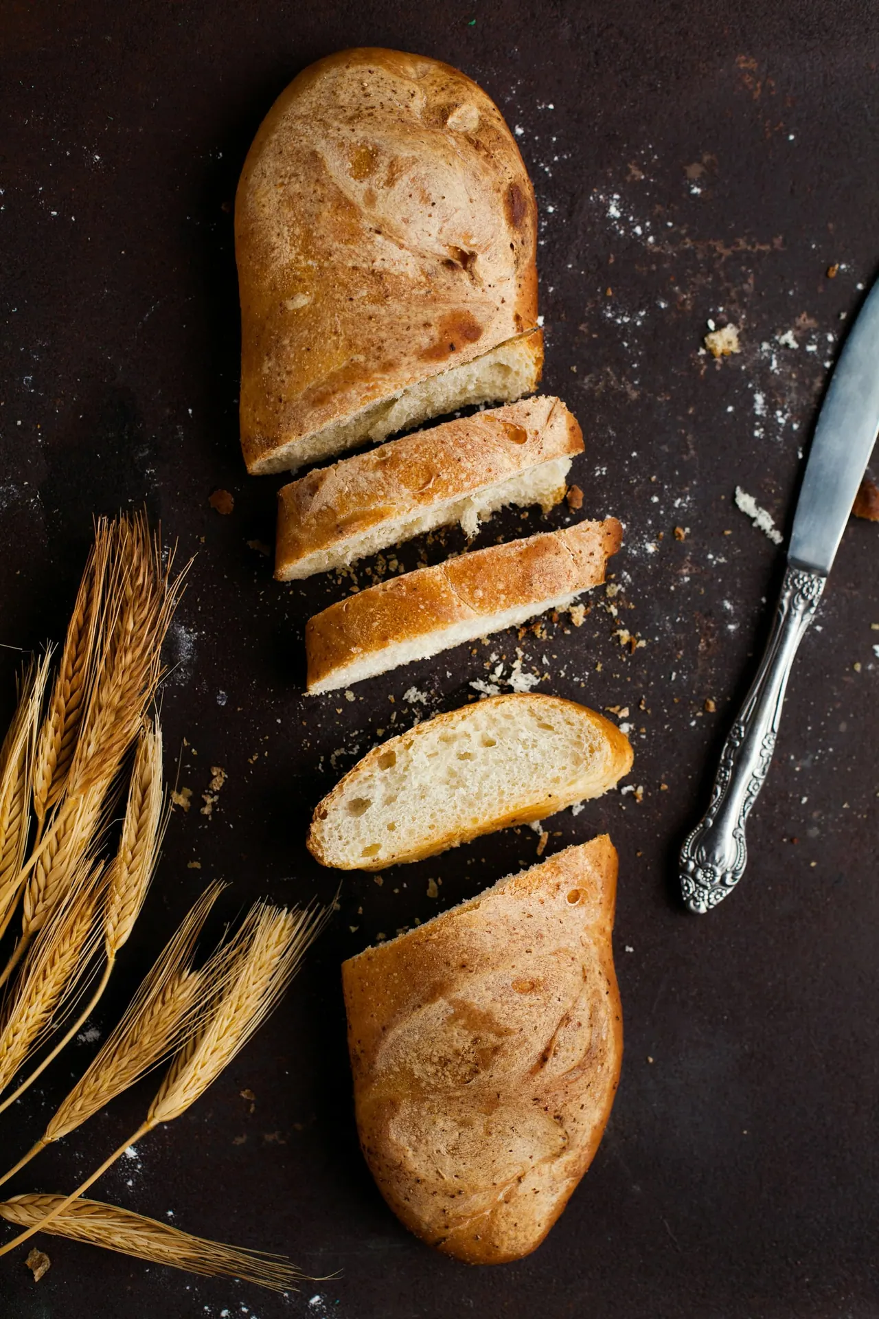 A sliced loaf beside a bread knife and wheat