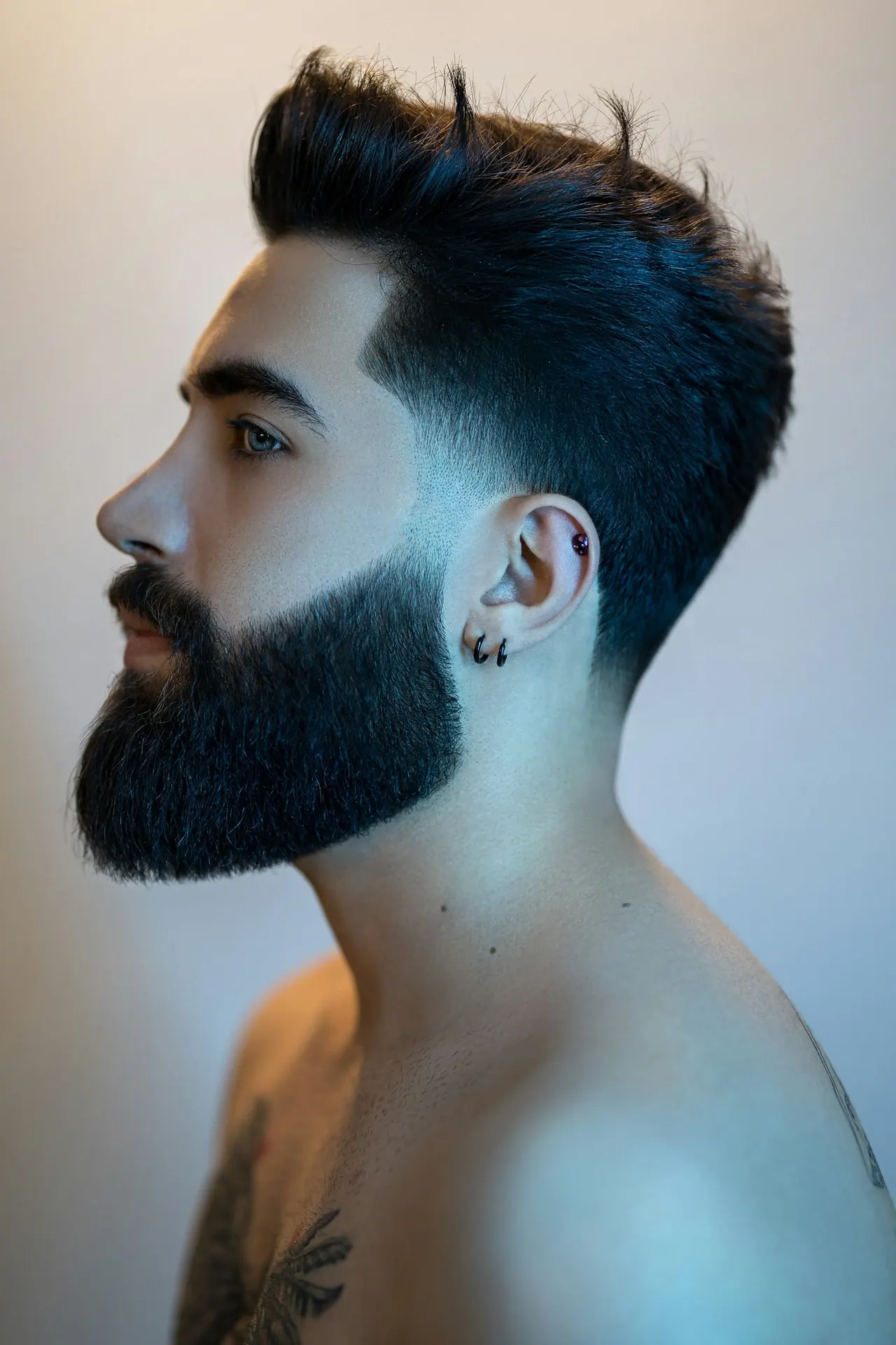 A man in profile with a high fade and a thick, sculpted beard