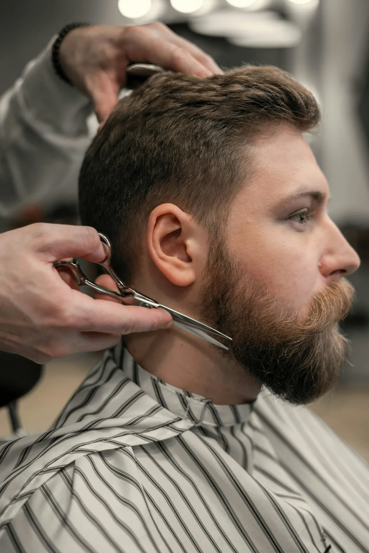 A barber trimming a client’s beard with scissors