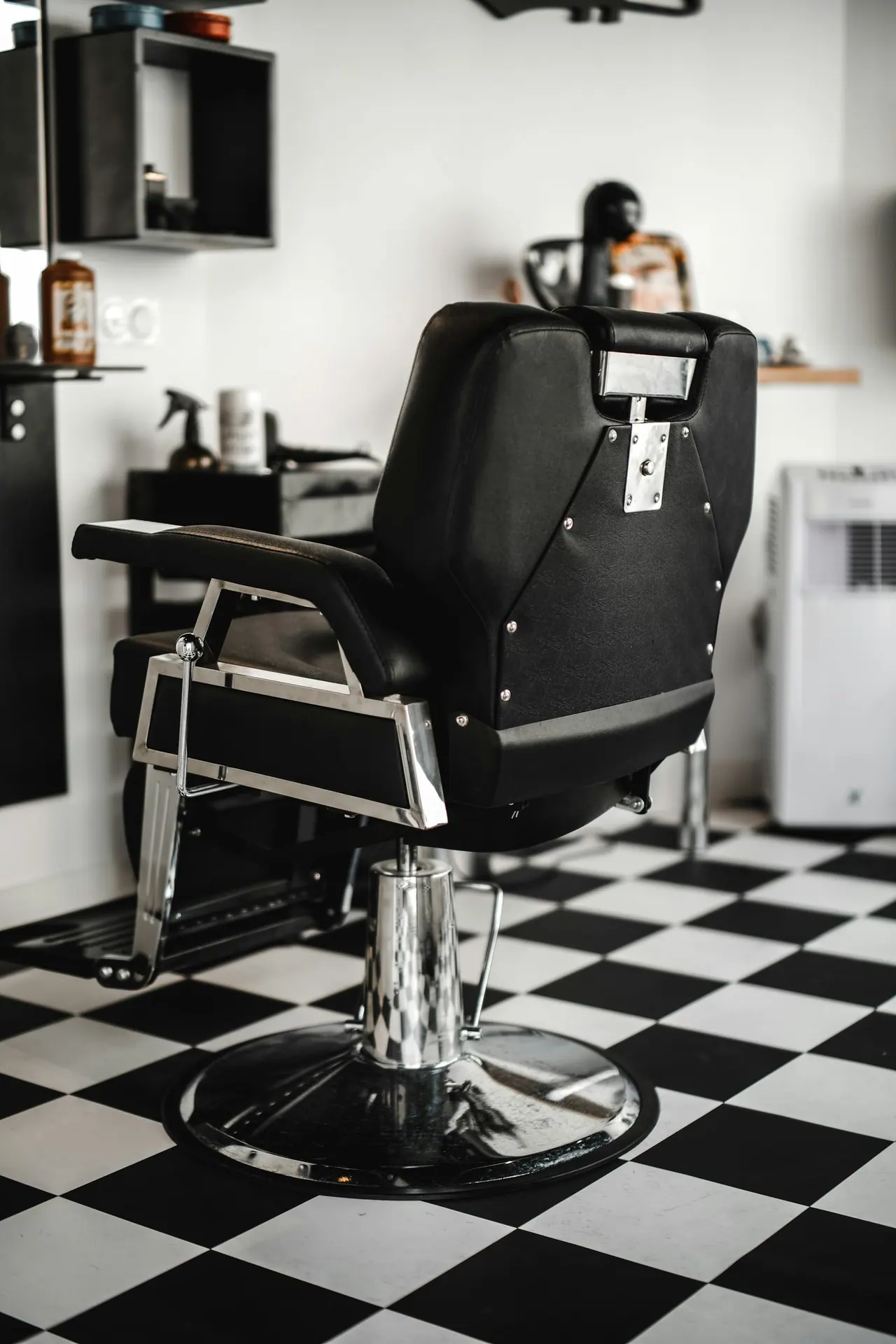 A black barber chair on a chequered floor in a bright shop