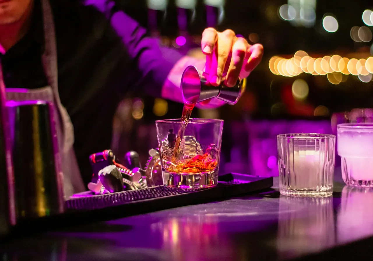 A bartender pouring a drink under violet light