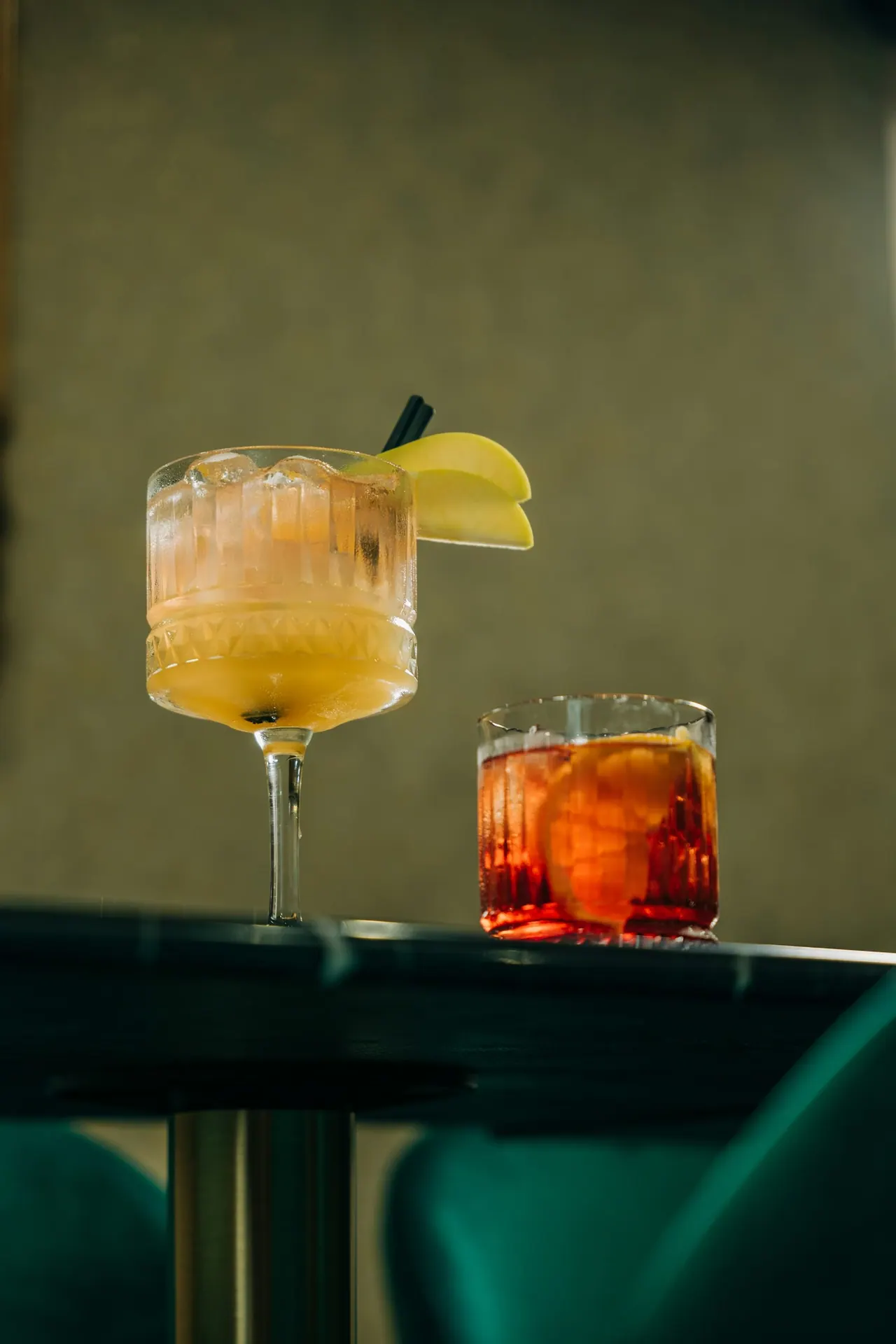 Two cocktails on a small table beside a green velvet banquette