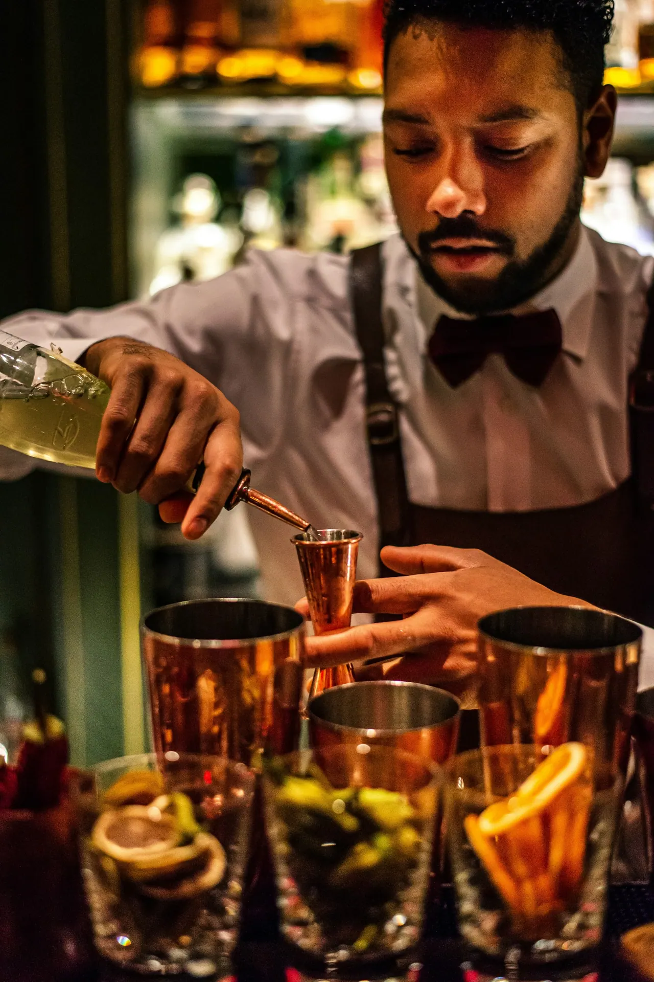 A bartender in a bow tie pouring drinks into copper cups at the bar