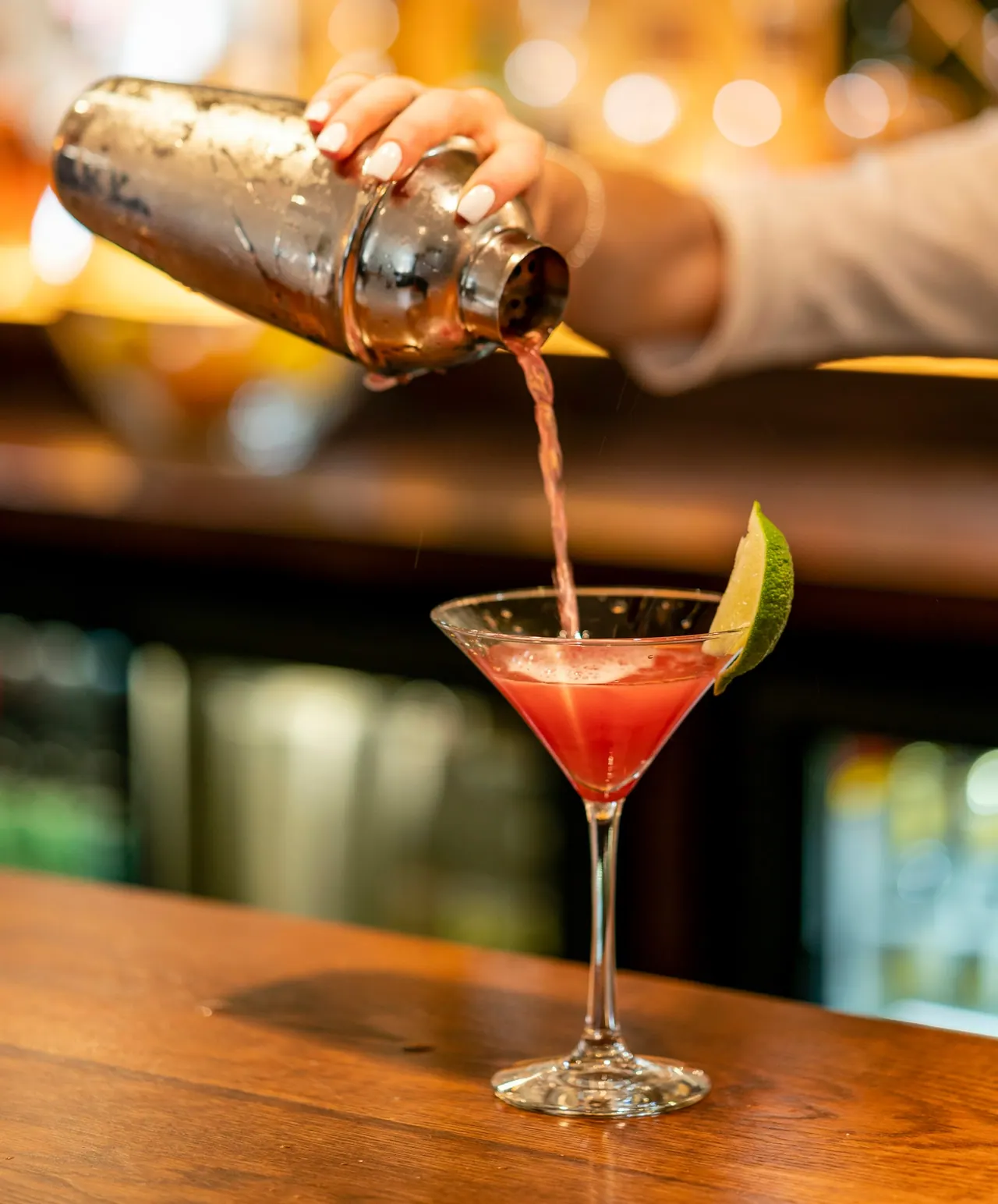 A pink cocktail poured from a shaker into a coupe