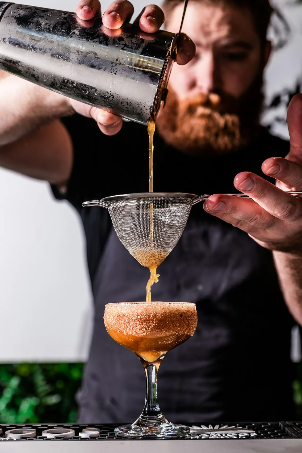 A bartender double straining a cocktail into a coupe