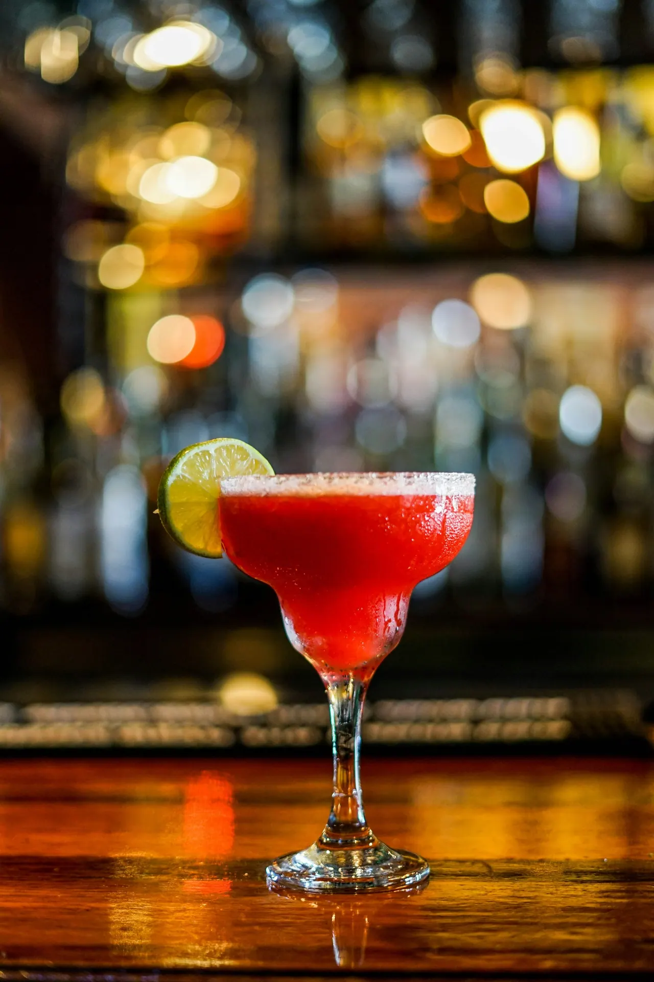 A red margarita on the bar with warm lights behind