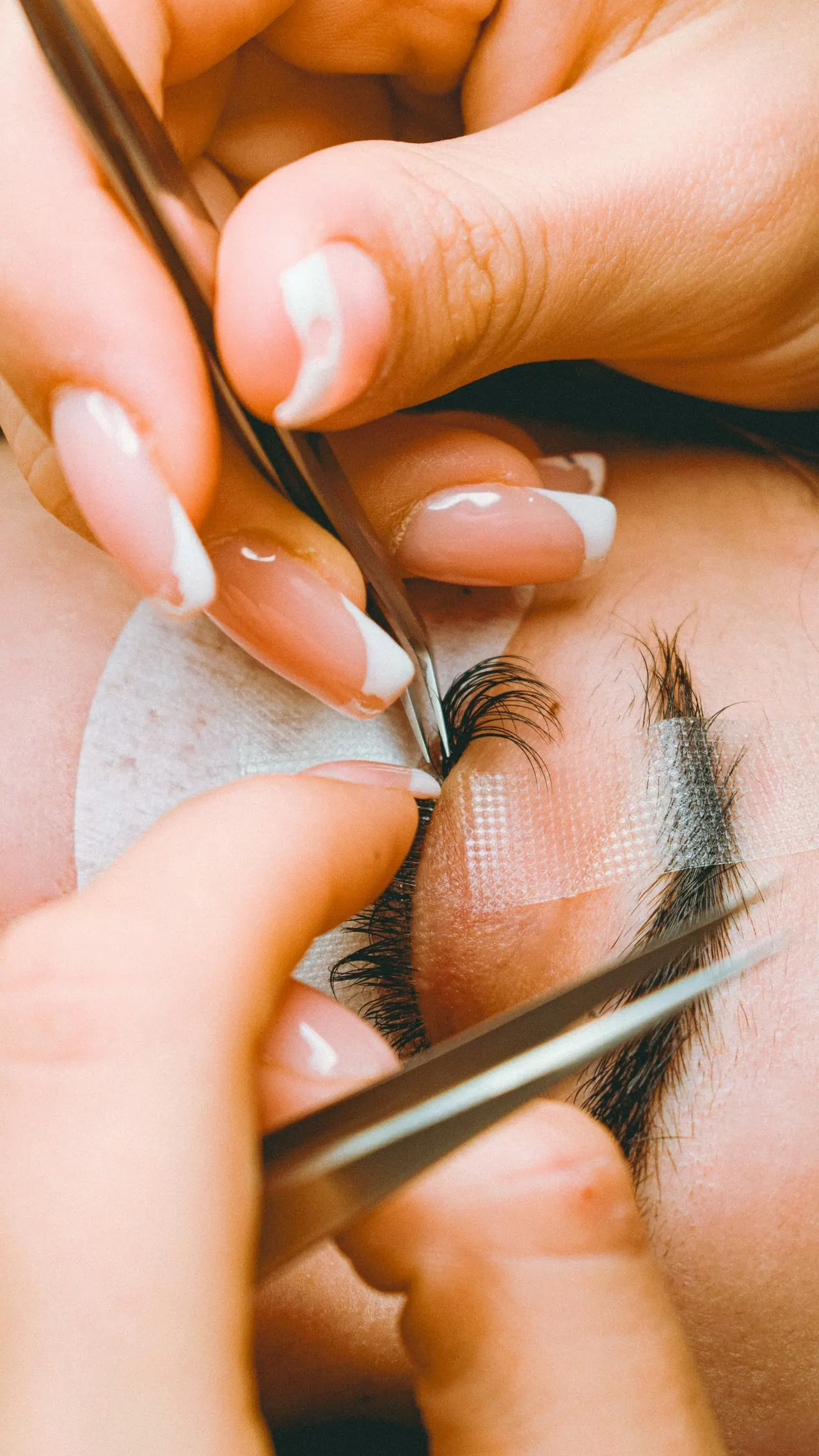 A lash artist placing extensions with two fine tweezers