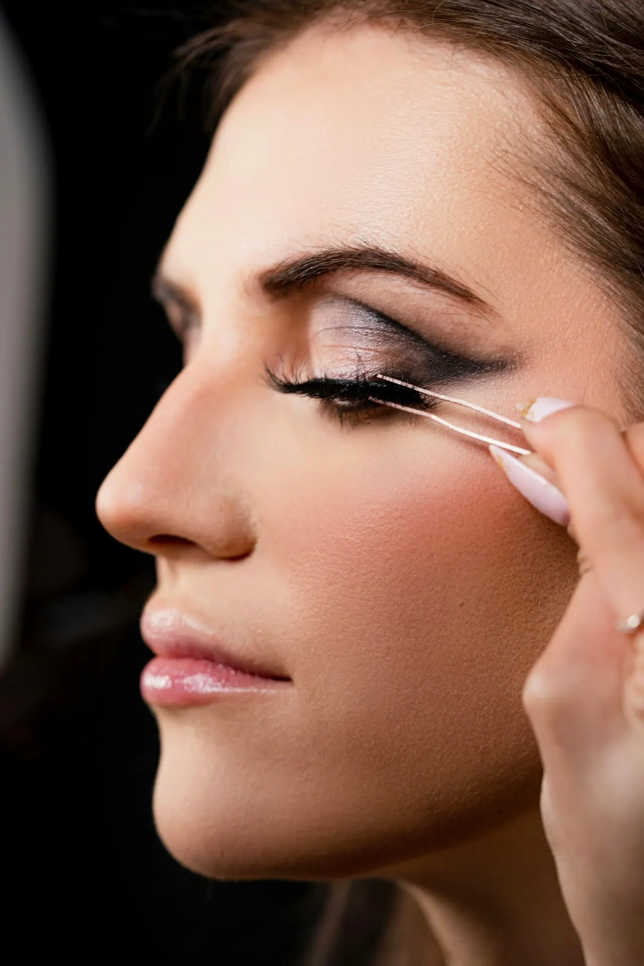 A makeup artist placing false lashes on a client in soft, low light