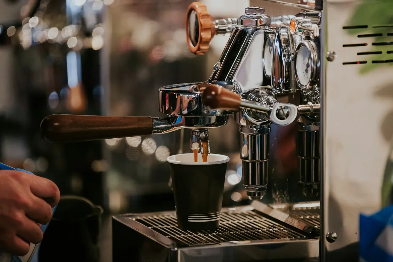 Espresso pouring from a chrome machine into a paper cup