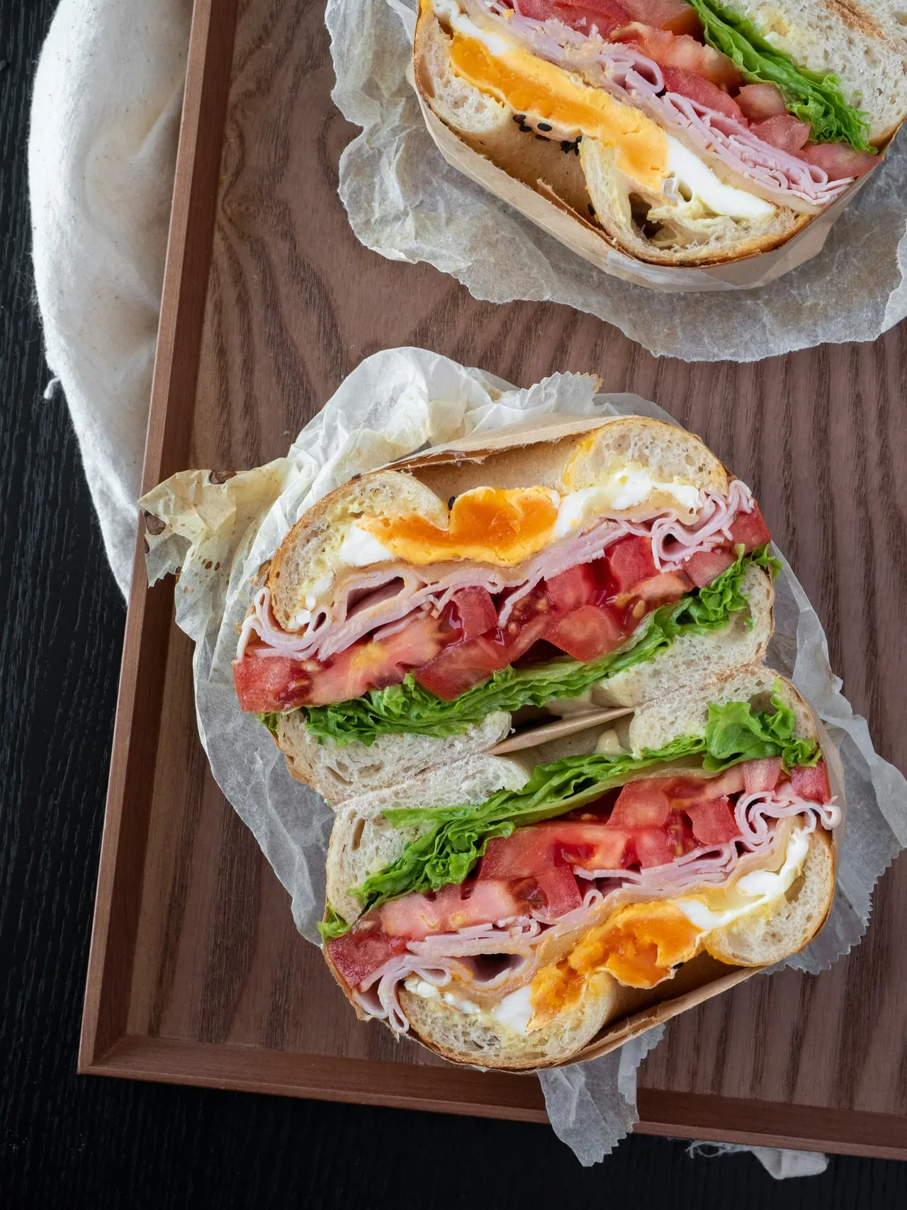 A bagel sandwich with egg, ham, tomato and greens