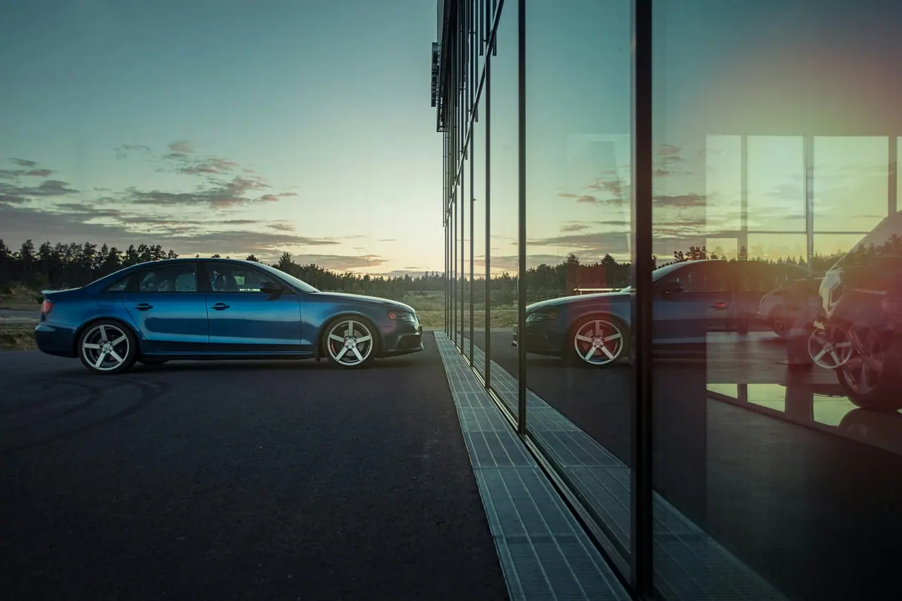 A blue midsize sedan beside a glass building at dusk