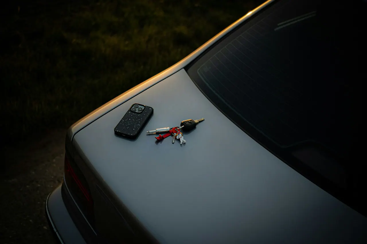 A phone and car keys resting on the trunk of a car at dusk