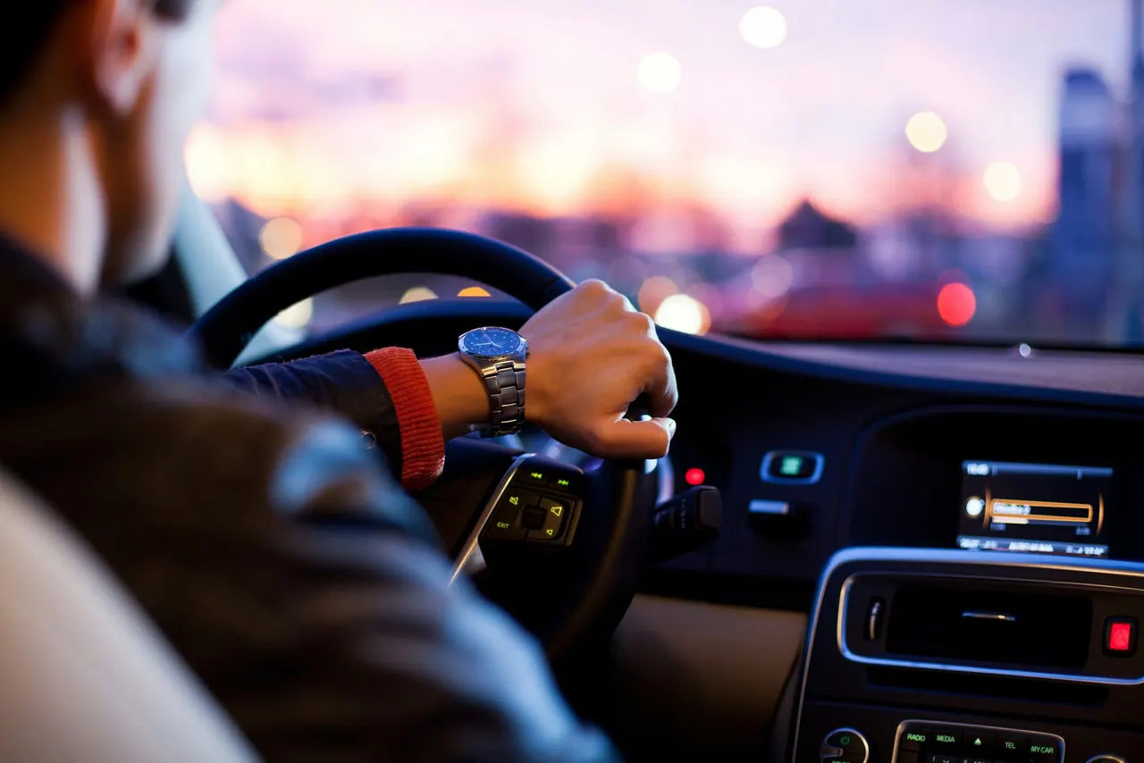 A hand on the steering wheel, driving through the city at dusk