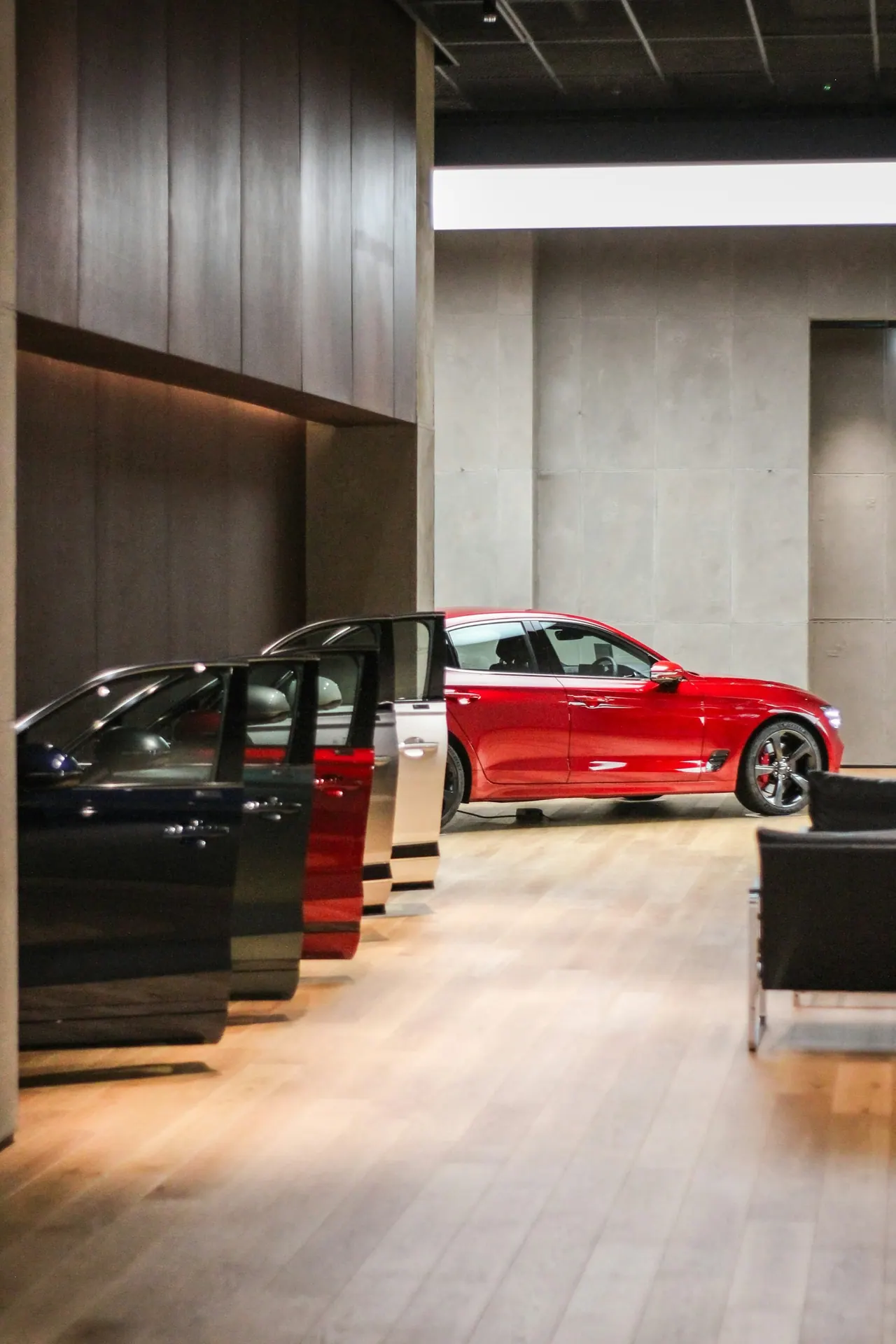 A showroom with a row of cars, doors open, and a red sedan in the light