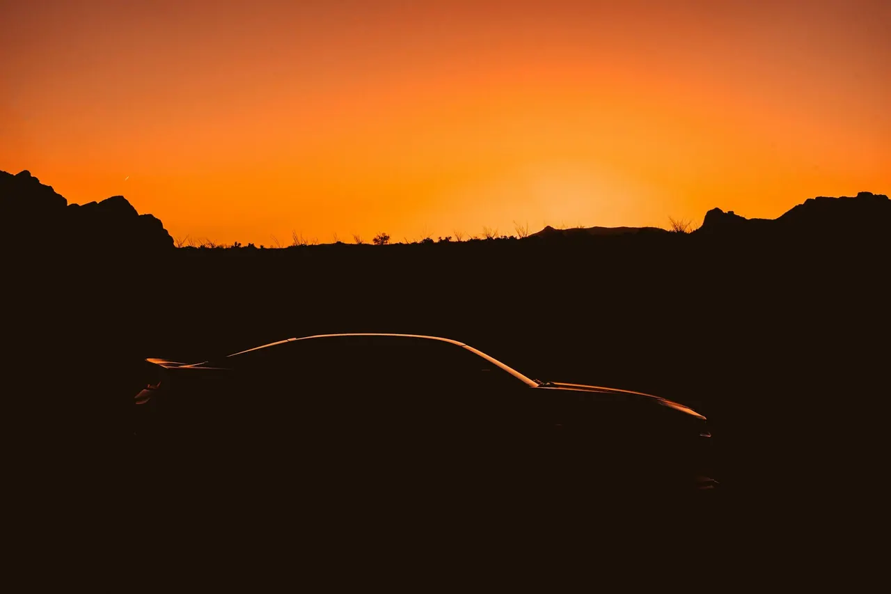 The silhouette of a sports coupe against an orange sunset