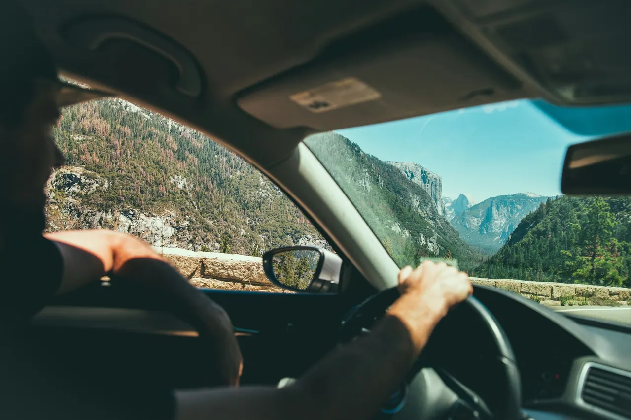 A hand on the wheel, driving through a green mountain valley