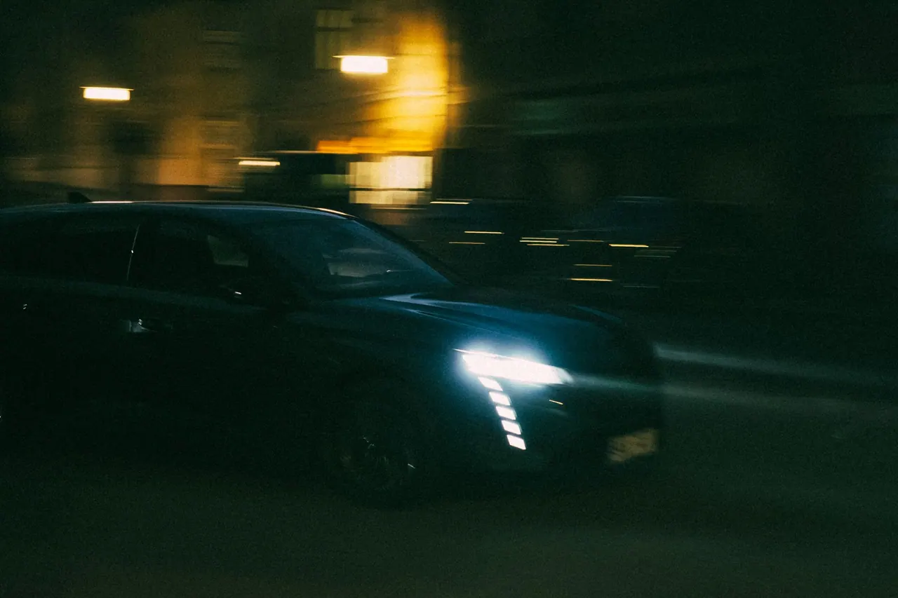A dark compact SUV on a city street at night, headlights on
