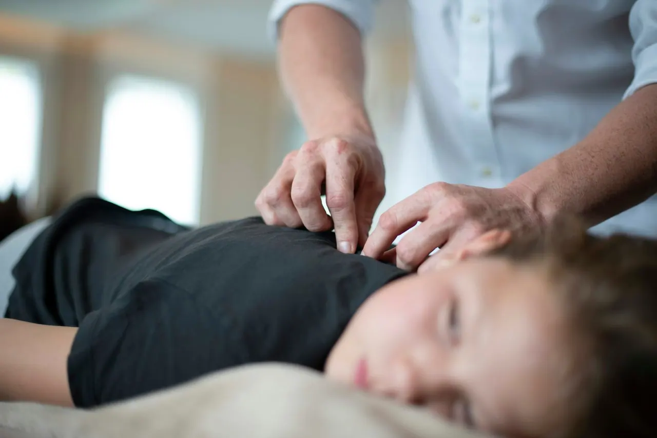 A chiropractor's hands on the upper back of a resting patient