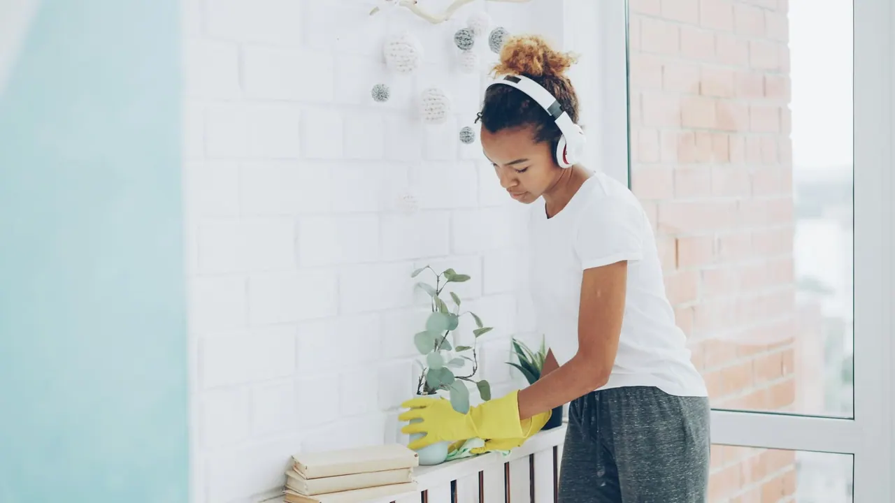 A cleaner in yellow gloves wiping a sunny windowsill