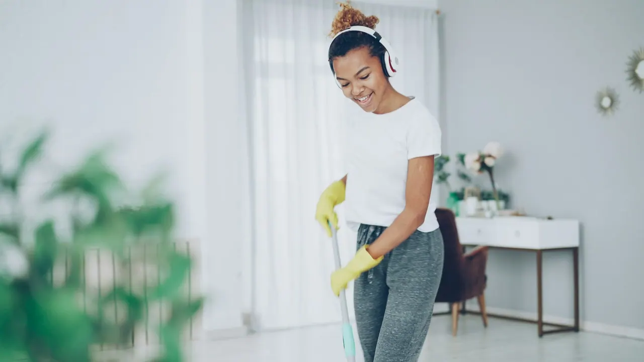 A smiling cleaner with headphones mopping a bright living room floor