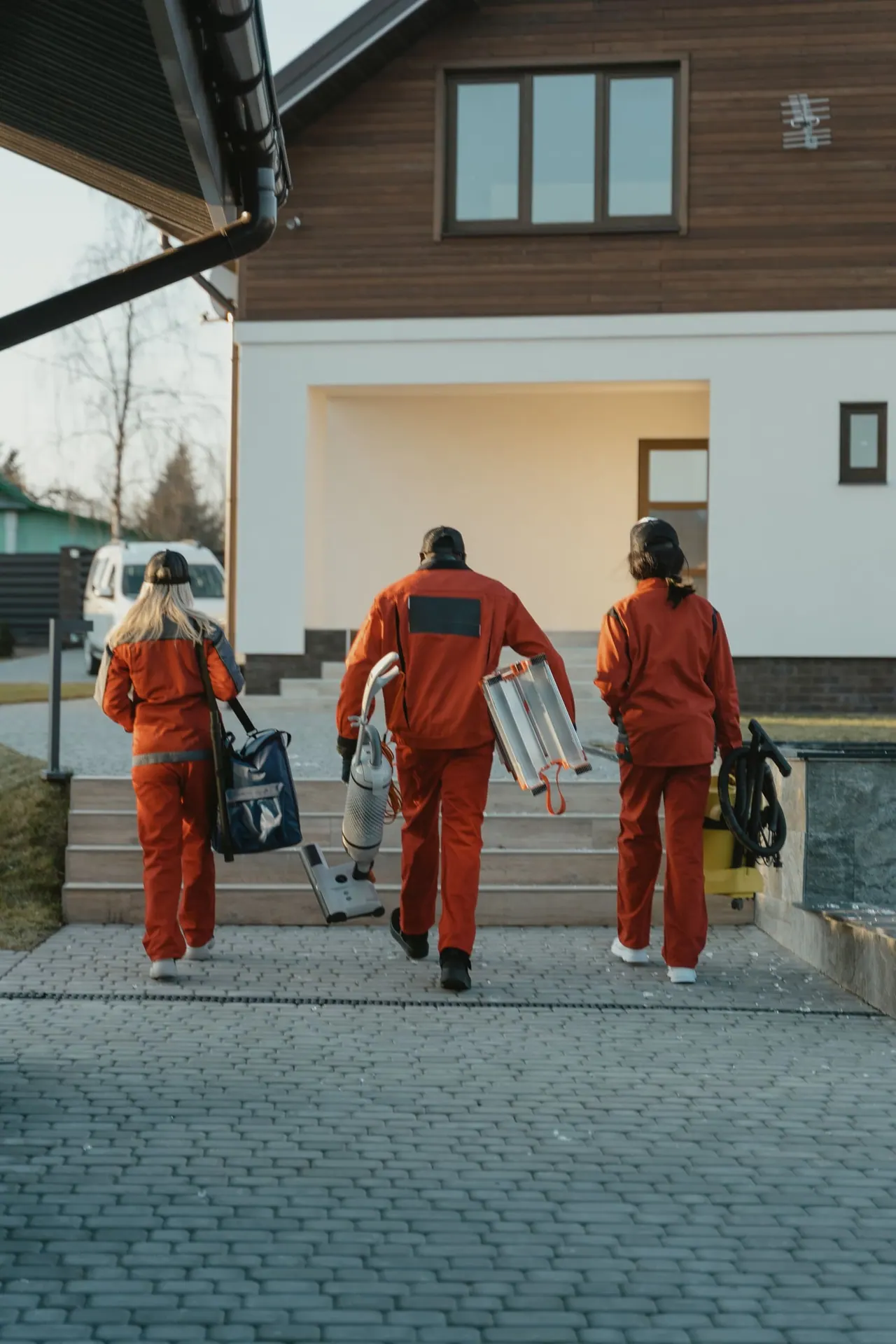 A cleaning crew in uniforms walking up to a modern home with their equipment