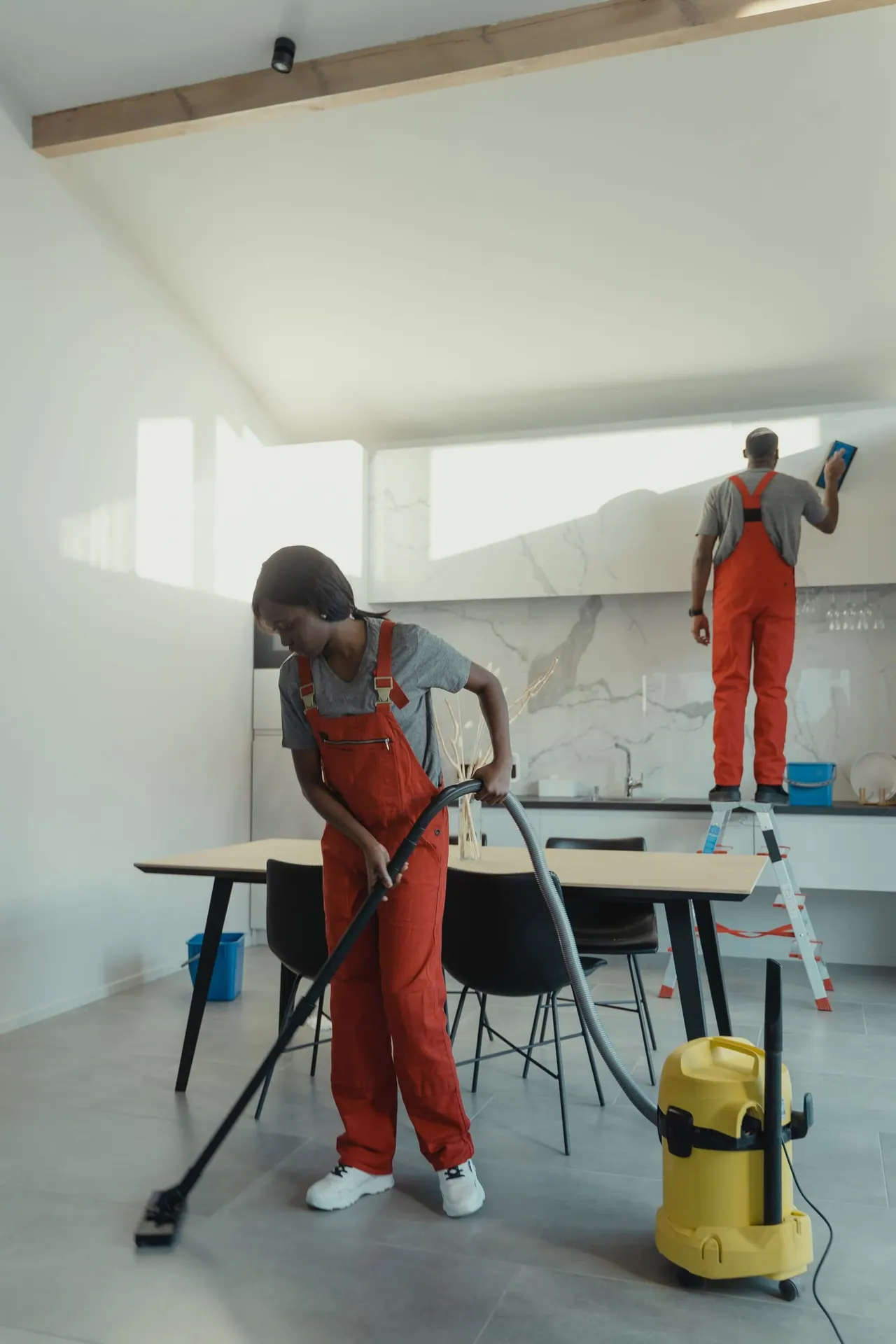 Two cleaners vacuuming and wiping a modern kitchen