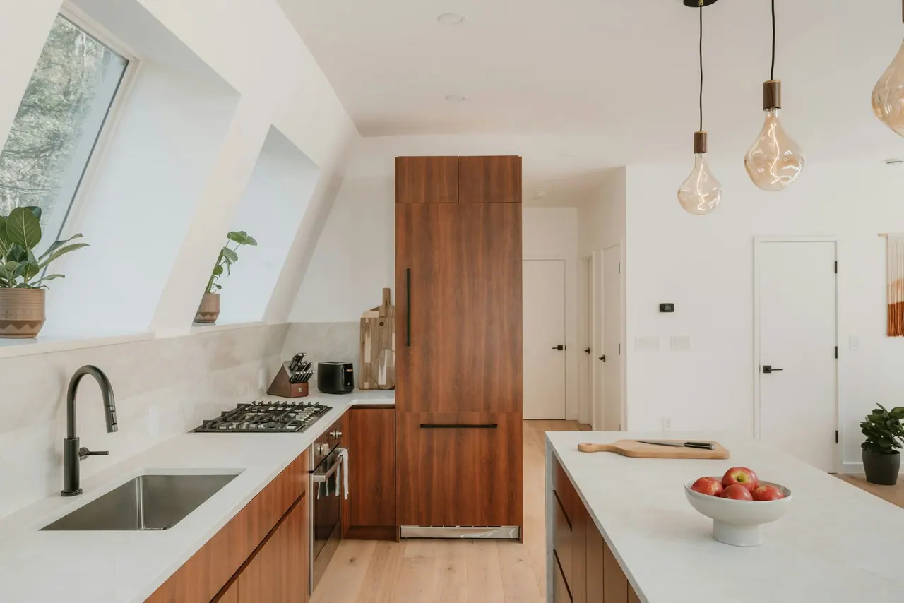 A modern kitchen with walnut cabinets, a white island and brass pendant lights