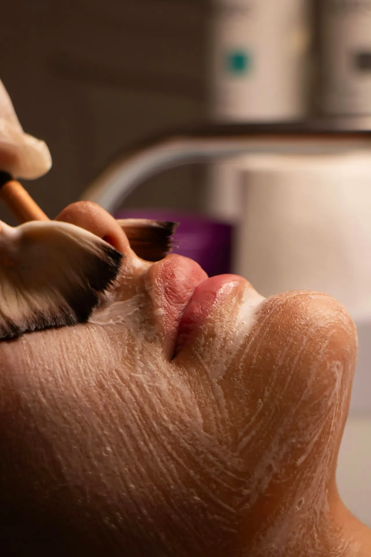 An esthetician brushing a soft cream mask across a guest’s face
