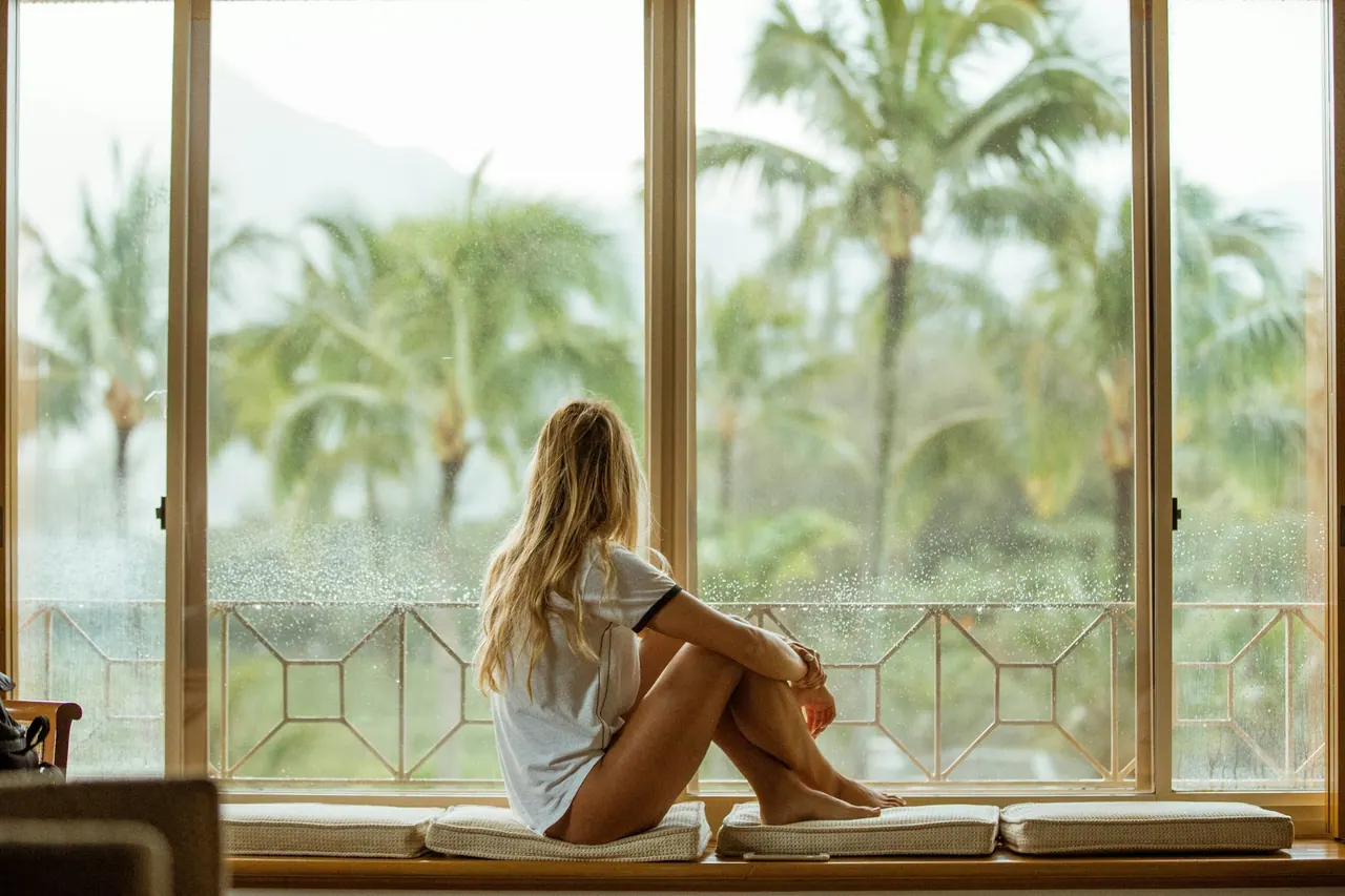 A guest resting on a window seat with a view of palm trees