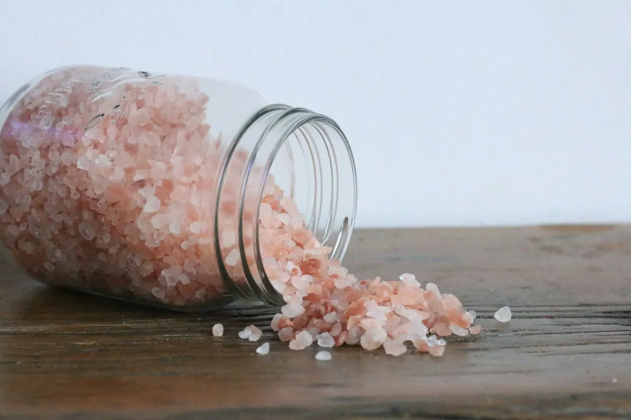 Pink bath salt spilling from a glass jar onto wood