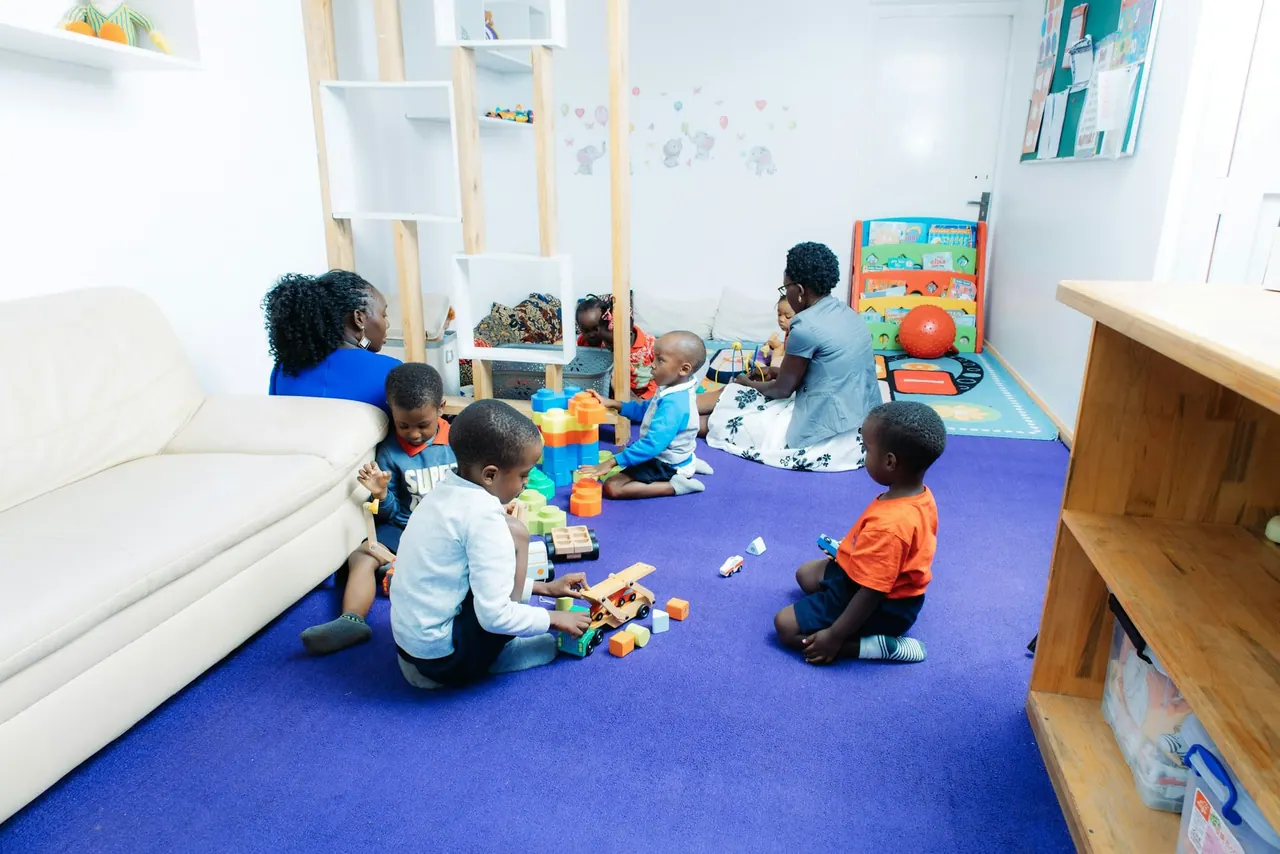 Children and teachers playing together on a blue carpet in a bright room