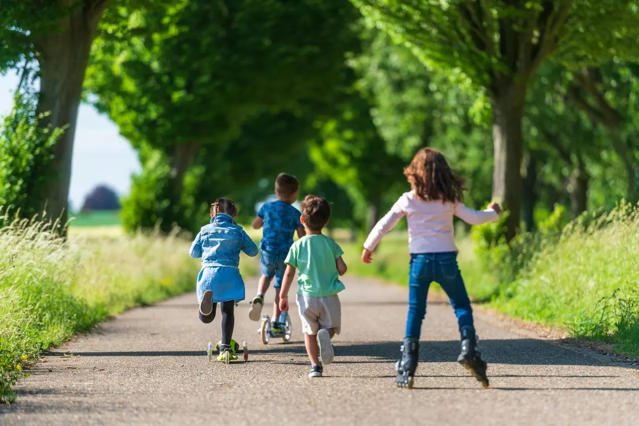 Children racing on scooters down a leafy park path