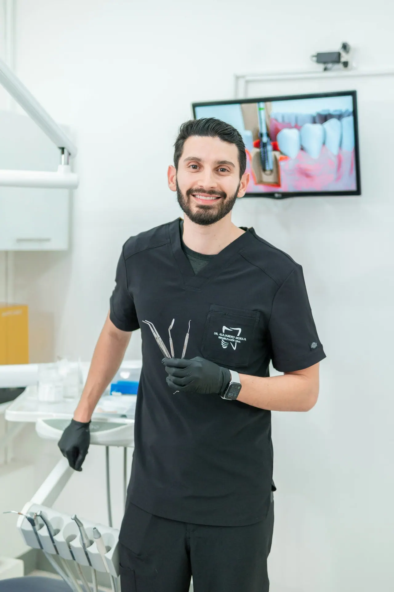 The lead dentist in black scrubs, smiling in a bright treatment room