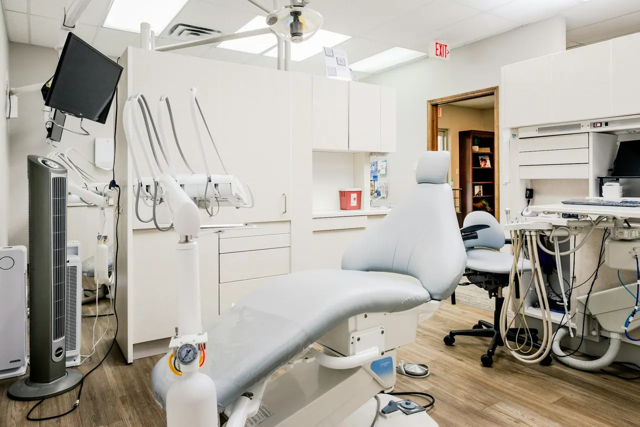 A modern treatment room with a dental chair, screens and white cabinets