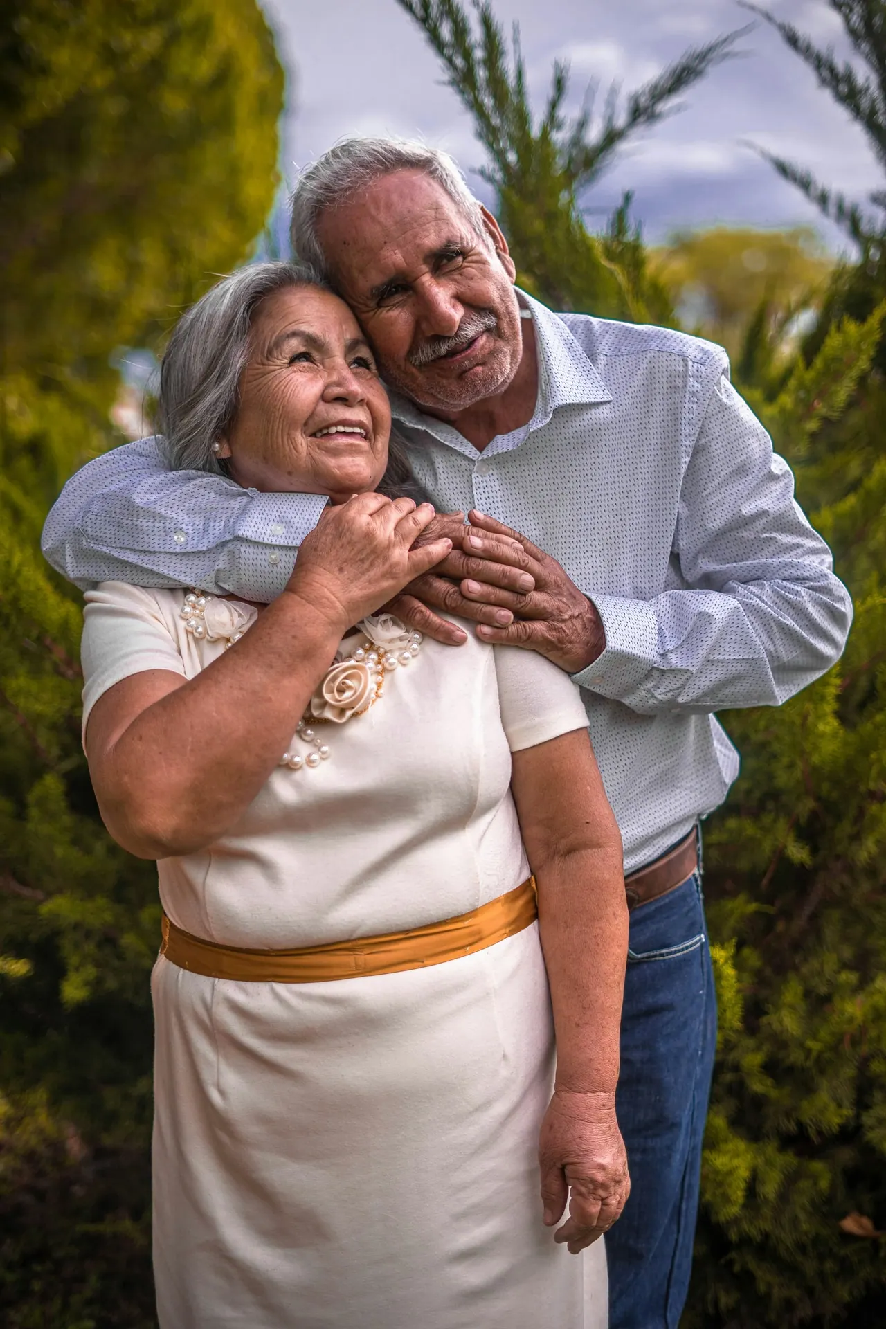An older couple embracing among evergreen trees, smiling