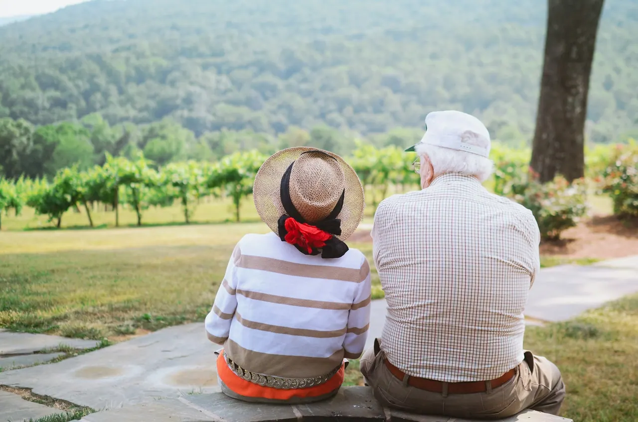 An older couple sitting side by side, looking out over green hills and vineyards