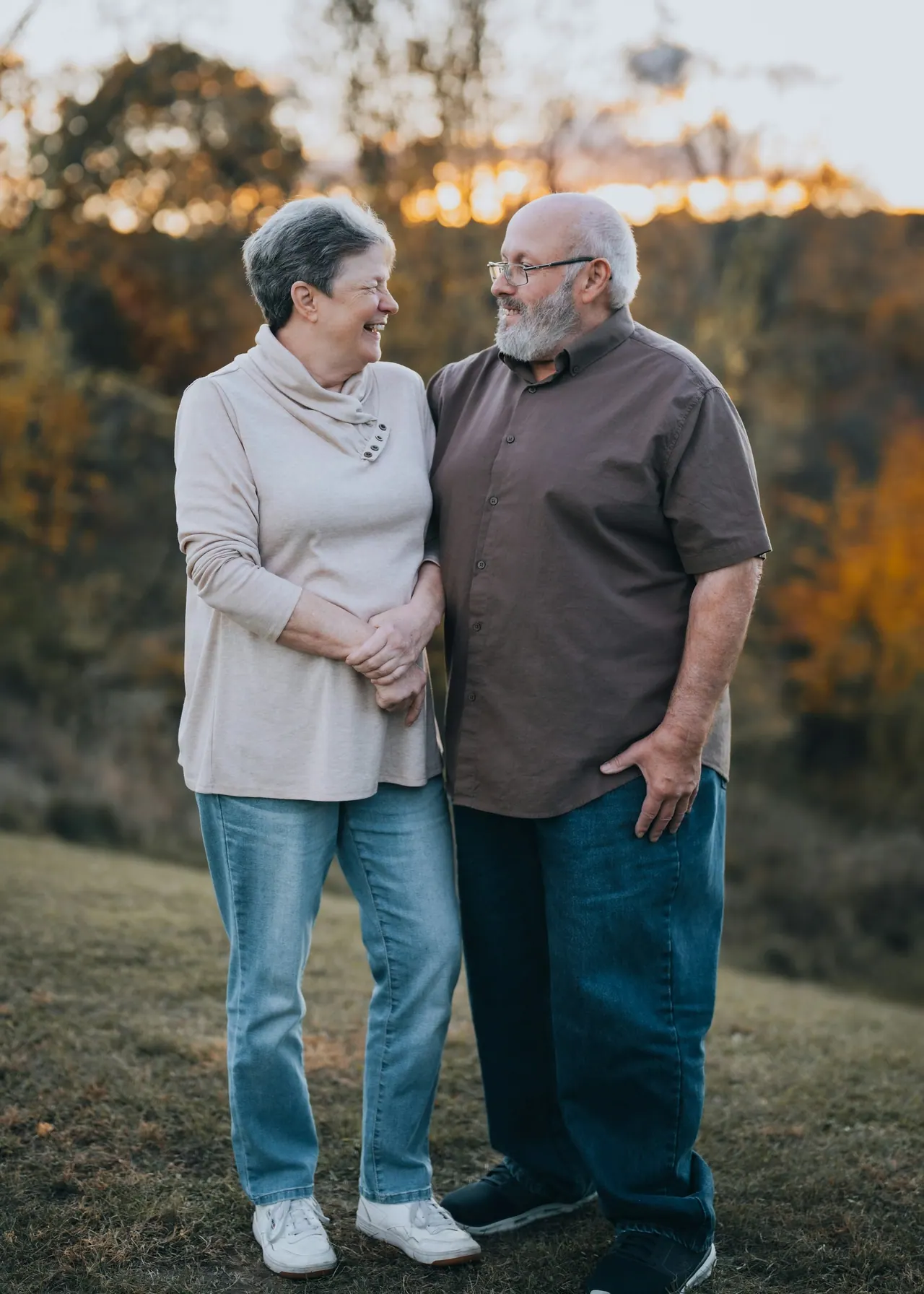 A smiling older couple standing arm in arm in a field at sunset