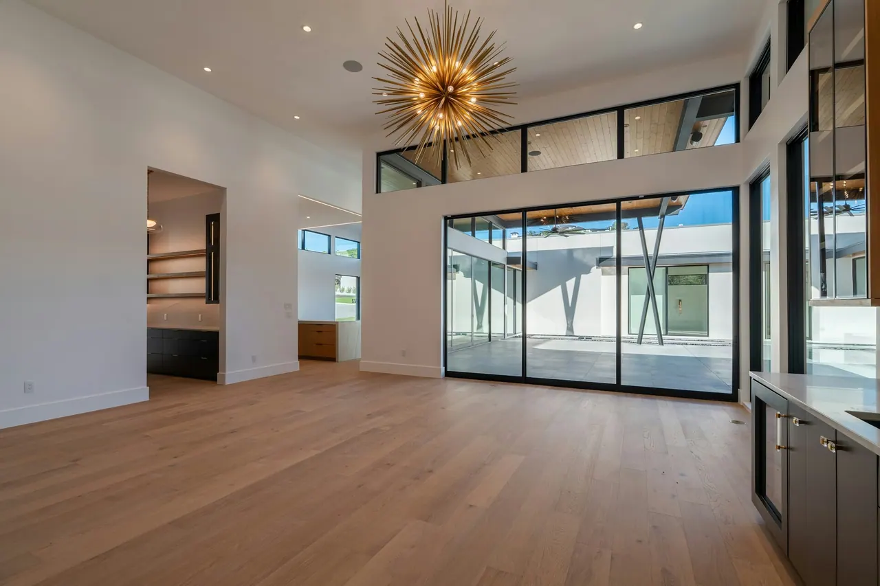 A bright empty room with new oak floors, tall glass doors and a starburst light