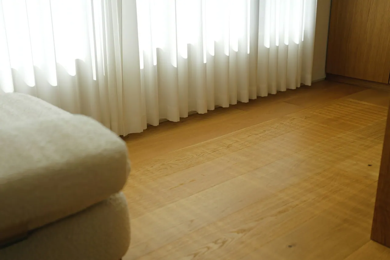 Soft daylight through sheer curtains over a warm wooden floor