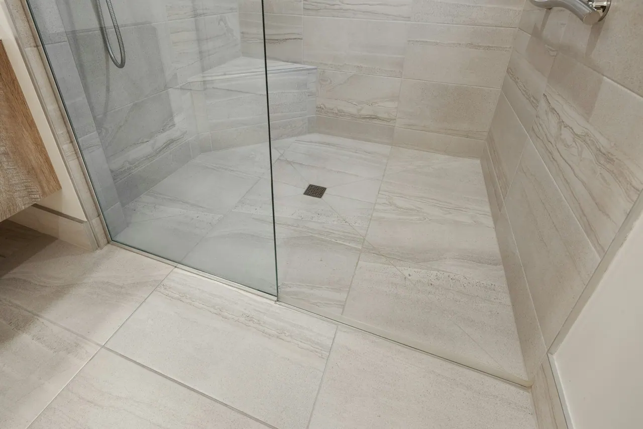A walk in shower lined with large pale stone tiles
