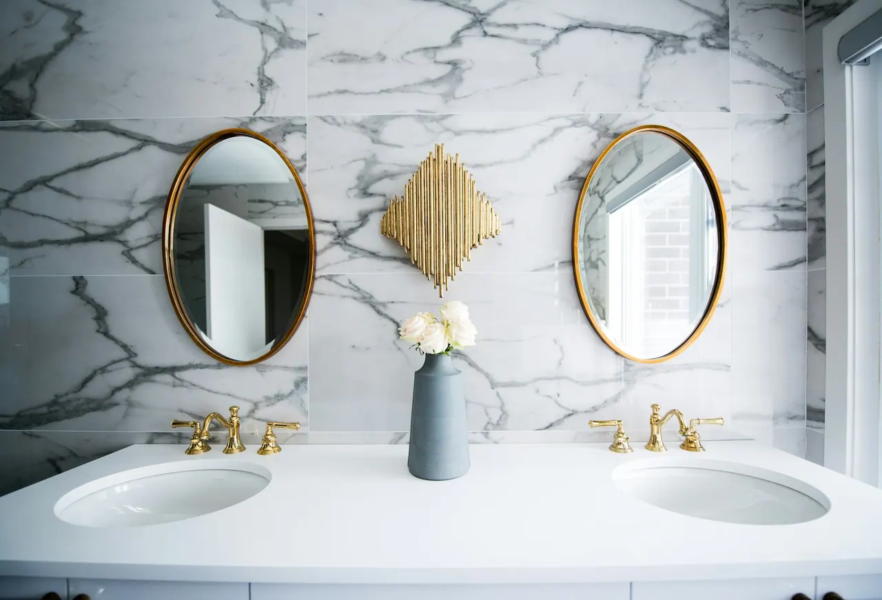 Marble wall tiles behind a double sink with brass mirrors