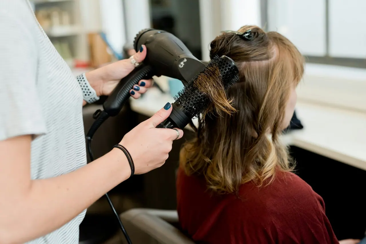 A stylist blow drying a client’s hair with a round brush
