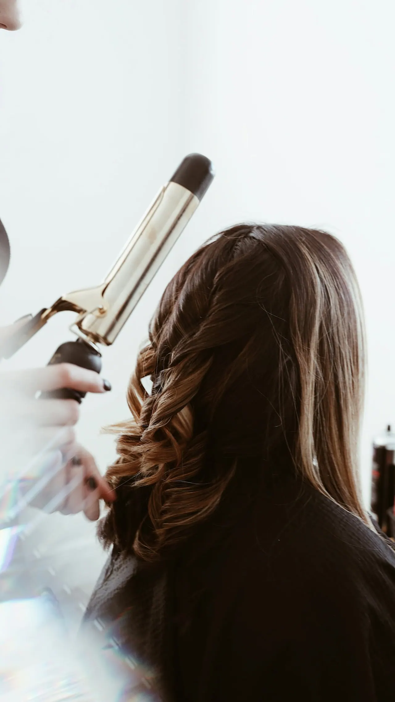 A stylist curling long brown hair with a curling iron