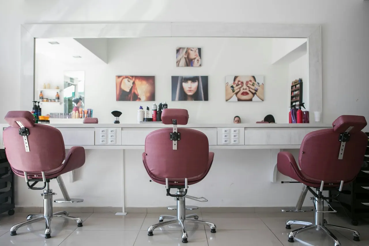 A bright salon with pink velvet styling chairs facing a long mirror